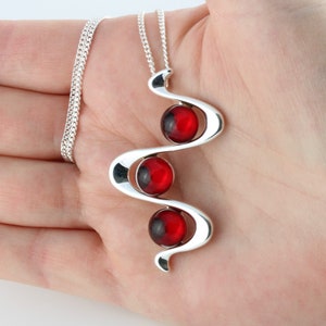 May include: A silver necklace with a pendant featuring three red glass beads set in a wavy design.