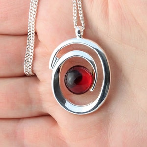 May include: A silver necklace with a red and black swirl pendant. The pendant is a circle with a smaller circle inside, and the smaller circle is spinning.