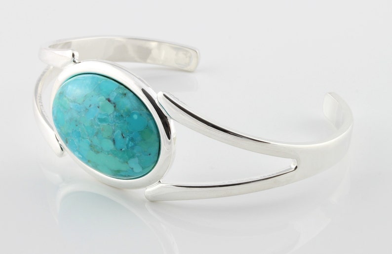 Pode incluir: Um bracelete de prata com uma pedra oval turquesa engastada no centro. O bracelete tem um design simples e moderno.