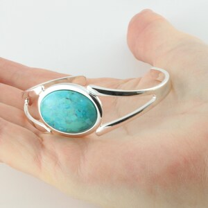 Pode incluir: Um bracelete de prata com uma pedra turquesa em caboch&atilde;o no centro.