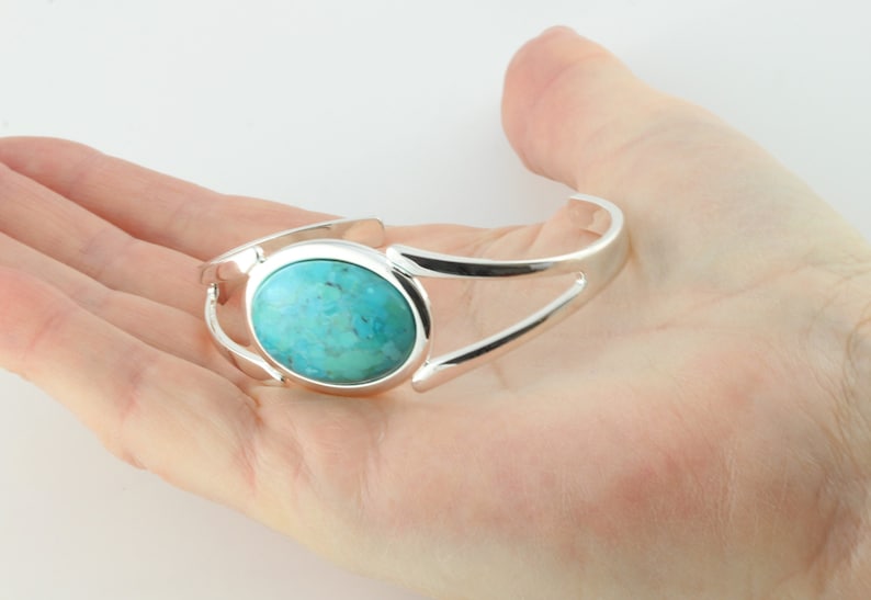 Pode incluir: Um bracelete de prata com uma pedra turquesa em caboch&atilde;o no centro.