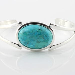 Pode incluir: Um bracelete de prata com uma pedra turquesa caboch&atilde;o engastada em uma moldura de prata.