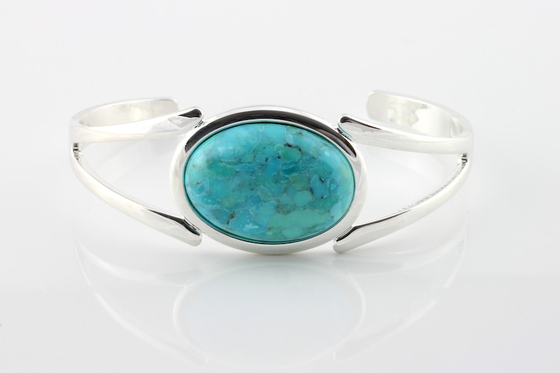 Pode incluir: Um bracelete de prata com uma pedra turquesa caboch&atilde;o engastada em uma moldura de prata.