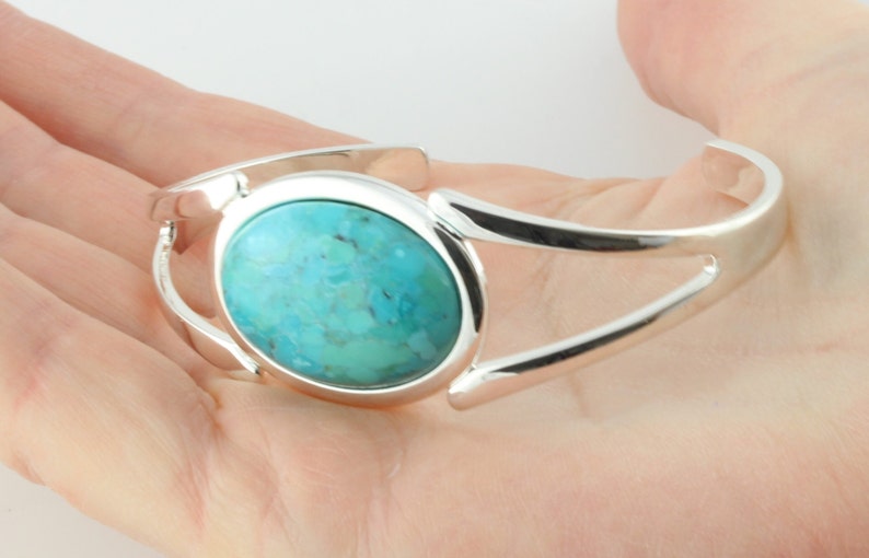 Pode incluir: Um bracelete de prata com uma pedra turquesa caboch&atilde;o engastada em um bezel circular.