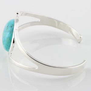 Pode incluir: Um bracelete de prata com uma pedra turquesa engastada no centro. O bracelete tem um design simples e aberto.