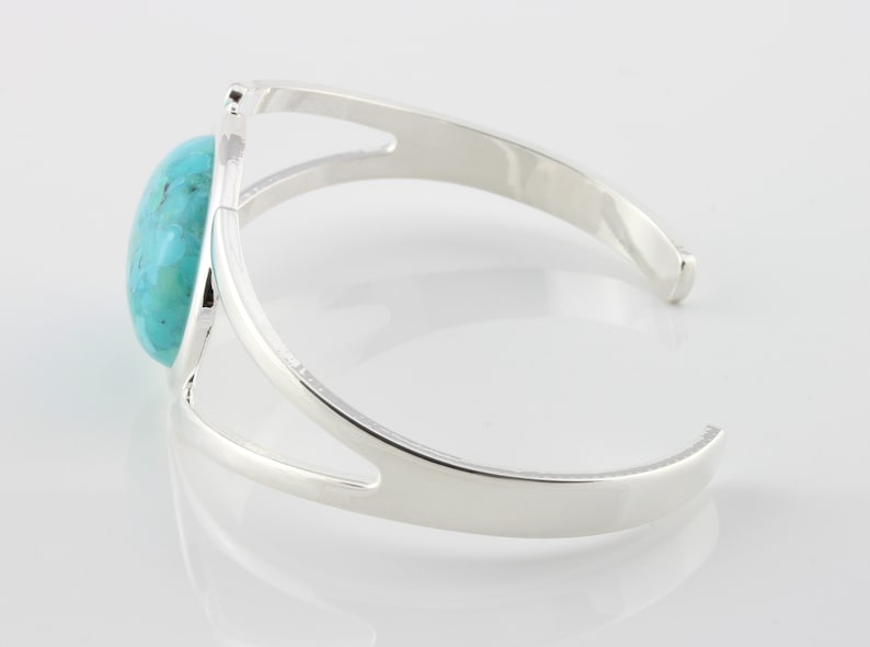Pode incluir: Um bracelete de prata com uma pedra turquesa engastada no centro. O bracelete tem um design simples e aberto.