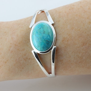 Pode incluir: Uma pulseira de prata com uma grande pedra oval turquesa engastada no centro. A pulseira tem um design simples e elegante.