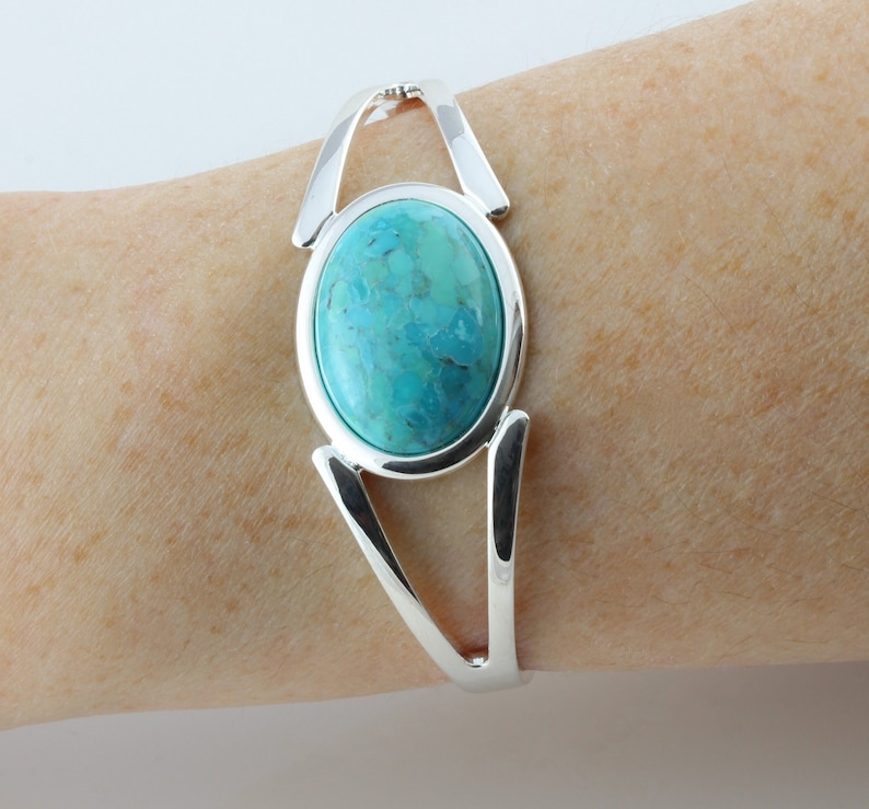 Pode incluir: Uma pulseira de prata com uma grande pedra oval turquesa engastada no centro. A pulseira tem um design simples e elegante.