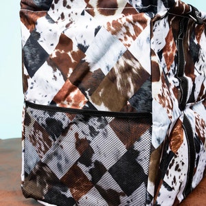 May include: A tote bag with a cowhide pattern in brown, black, and white. The bag features a mesh pocket on the front and is designed with a diamond pattern. The bag is made of a durable material and is suitable for carrying various items.