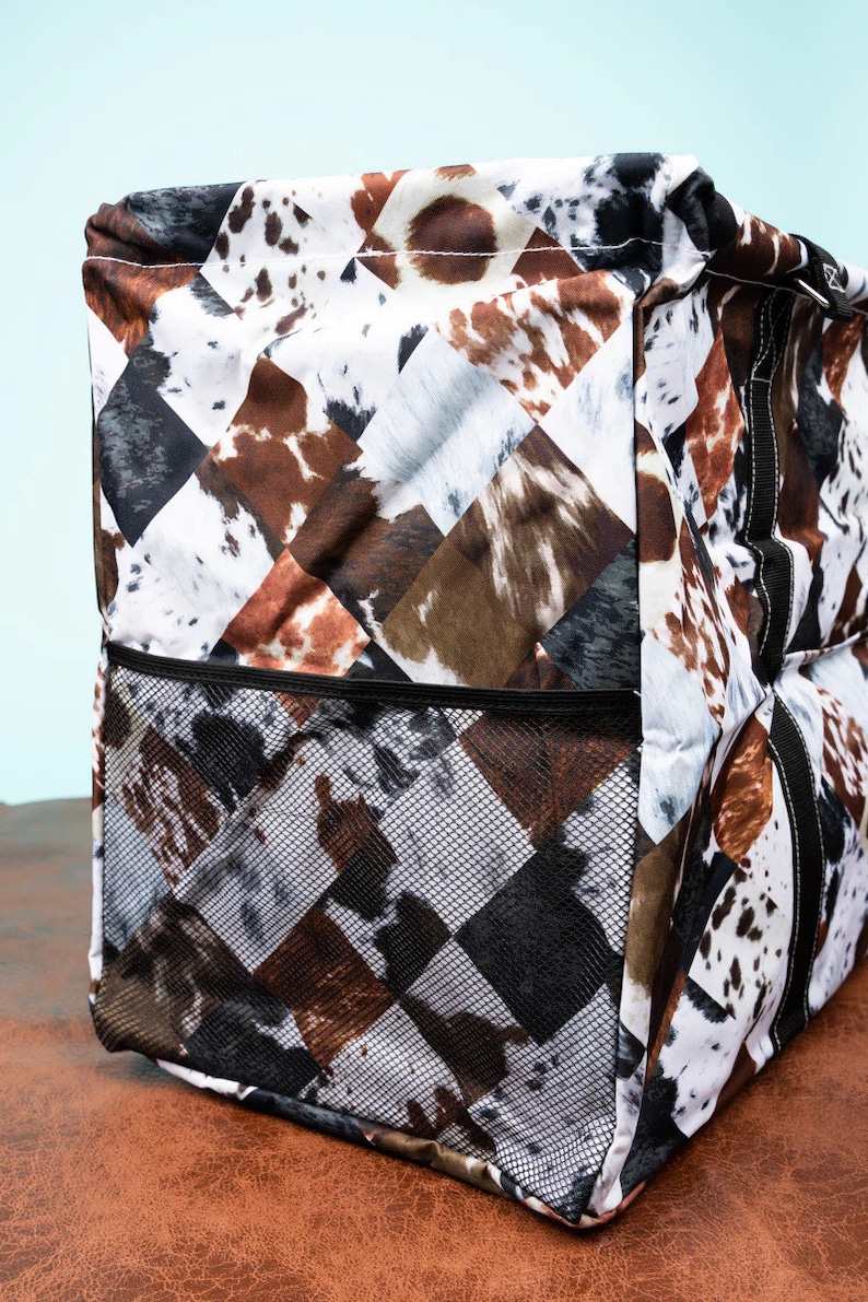 May include: A tote bag with a cowhide pattern in brown, black, and white. The bag features a mesh pocket on the front and is designed with a diamond pattern. The bag is made of a durable material and is suitable for carrying various items.