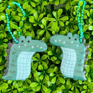 May include: Two green alligator keychains with a light blue and white pattern. The keychains are hanging from a green chain.