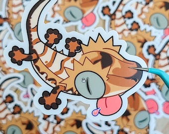 May include: A sticker of a cartoon lizard with a spiky back, brown and white stripes, and a pink tongue sticking out. The lizard is on a white background.