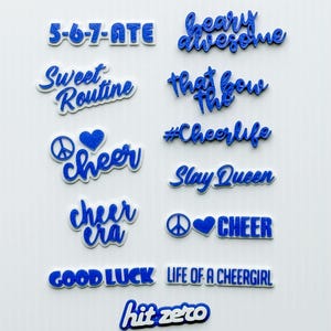 May include: A collection of blue and white decorative word cutouts with phrases like "5-6-7-ATE", "heavy awesome", "Sweet Routine", "Cheer", "Slay Queen", and "Good Luck". The cutouts are in a variety of fonts and styles.