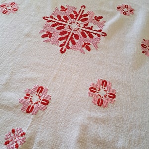 May include: White tablecloth with red and pink embroidered floral designs. The tablecloth has a central large floral design and smaller floral designs around the edges.