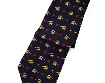 Puede incluir: Una corbata de seda azul oscuro con un patrón repetido de figuras de animales doradas y flores rojas.