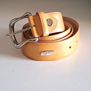 May include: A yellow leather belt with a silver buckle. The belt is rolled up and the buckle is visible.