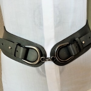 May include: A wide grey leather belt with two large silver D-shaped buckles connected by a chain.