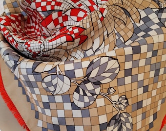 May include: A square silk scarf with a geometric pattern in red, white, tan, and gray. The scarf features a grid design with leaf and floral motifs. The edges are trimmed with a bright red fringe.