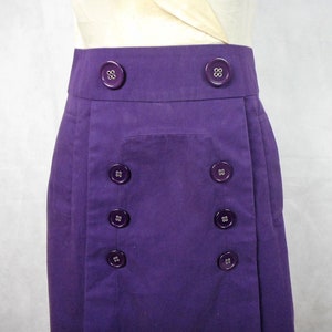 May include: A purple skirt with a front pocket and a row of buttons down each side.