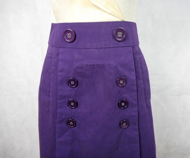 May include: A purple skirt with a front pocket and a row of buttons down each side.