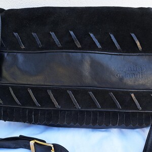 May include: A black handbag featuring a combination of smooth leather and suede textures. The front flap displays decorative leather lacing details and a fringe trim. The brand name valentino orlandi is embossed on the leather section. A black shoulder strap with a gold-tone metal buckle is attached.