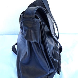 May include: A black leather shoulder bag featuring a fold-over flap with a textured suede panel and vertical stitched detailing. The bag includes a long, adjustable shoulder strap and a smooth leather body with a soft, slouchy construction.