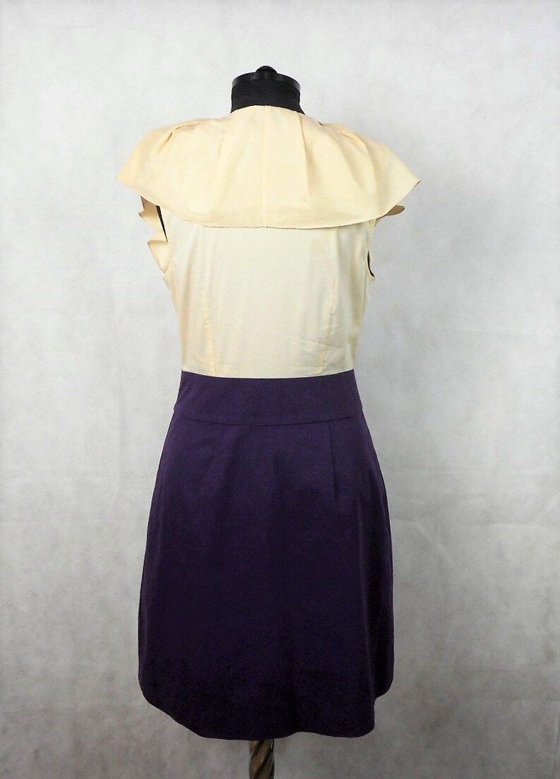May include: A sleeveless dress with a yellow top and a purple skirt. The top has a large ruffle collar.
