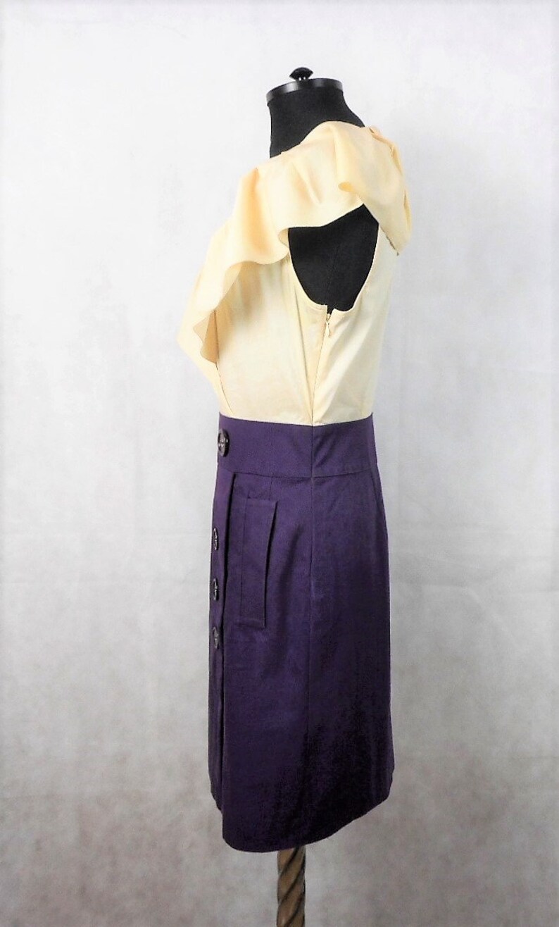 May include: A yellow and purple dress with a ruffled neckline and a button-up front. The dress has a fitted bodice and a skirt that falls to the knee.