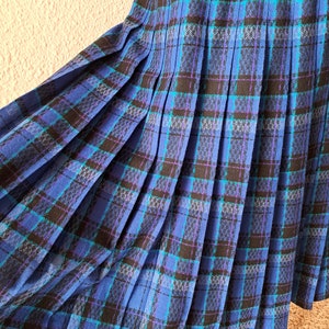 Pode incluir: Uma saia azul xadrez com detalhes em preto e roxo. A saia é plissada e tem uma silhueta fluida.