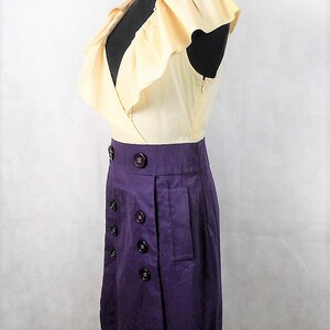 May include: A sleeveless dress with a ruffled, cream-colored bodice and a purple skirt. The skirt has a double row of buttons and a pocket on the side.