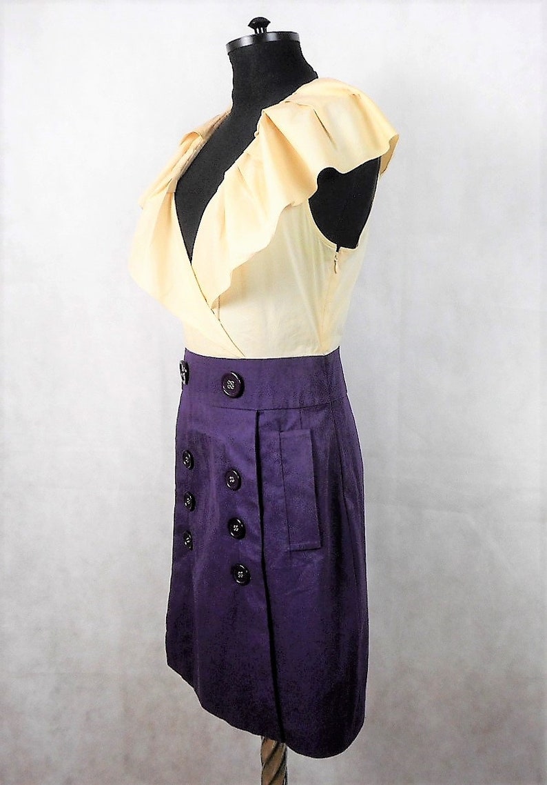 May include: A sleeveless dress with a ruffled, cream-colored bodice and a purple skirt. The skirt has a double row of buttons and a pocket on the side.
