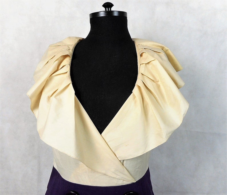 May include: A white ruffled collar with a V-neckline on a dress. The dress is a two-tone design with a purple bottom and a white top.