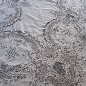 May include: A white tablecloth with intricate embroidered floral patterns. The design features delicate flowers, leaves, and swirls, creating a classic and elegant look.