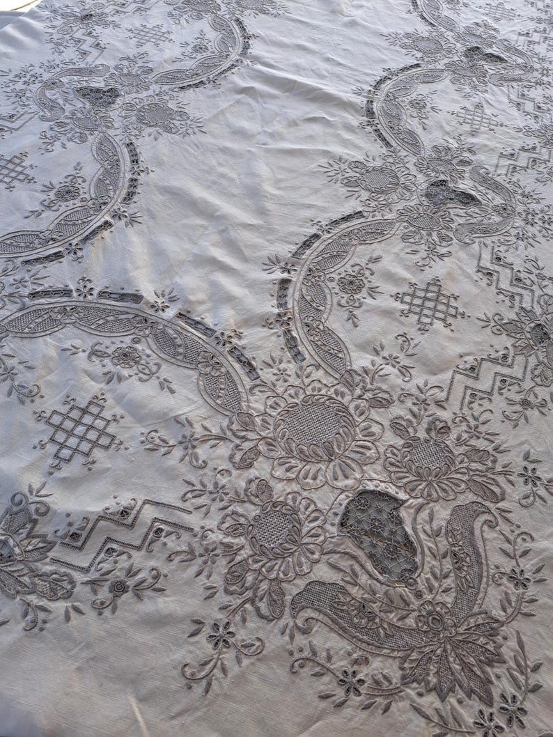 May include: A white tablecloth with intricate embroidered floral patterns. The design features delicate flowers, leaves, and swirls, creating a classic and elegant look.