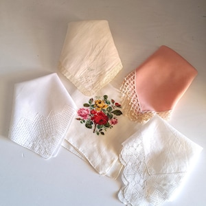 May include: Four white handkerchiefs with lace trim. One handkerchief features a floral embroidery design, another has a cursive inscription, and two have a simple lace border.
