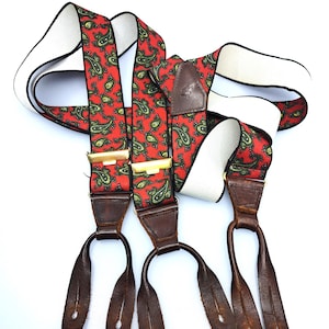 Può includere: Bretelle con motivo paisley rosso e verde con cinturini in pelle marrone e clip in metallo dorato.