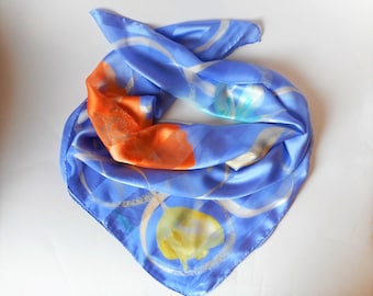 May include: A blue silk scarf with a white, orange, and yellow abstract design. The scarf is folded and laid flat on a white surface.