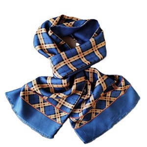 May include: A blue scarf with a plaid pattern in tan and brown. The scarf has a solid blue border and fringe at the ends. The scarf is made of a silky material.