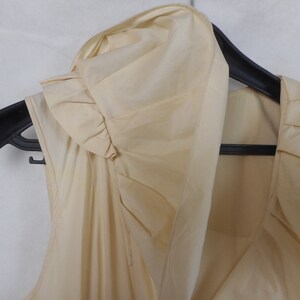 May include: A sleeveless, cream-colored blouse with a ruffled neckline and a draped design.