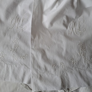 Op de afbeelding: Twee witte linnen kussenslopen met geborduurde bloemenmotieven en de initialen "ML" in een schrijflettertype.