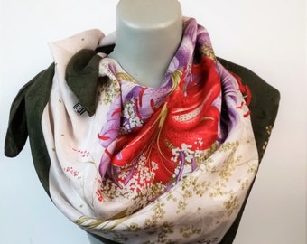 Könnte beinhalten: Ein Seidentuch mit einem Blumendesign, das eine große rote Lilie mit violetten und weißen Akzenten zeigt. Das Tuch ist gefaltet und auf dem Hals einer Schaufensterpuppe ausgestellt. Das Tuch hat einen dunkelgrünen Rand.
