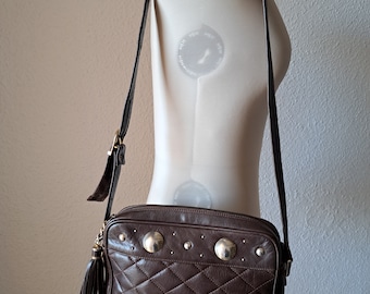 May include: A brown quilted leather shoulder bag with silver-toned studs and a gold tassel. The bag has a long adjustable strap.