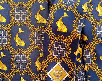 May include: A blue silk tie with a gold chain pattern and yellow fish. The tie has a white diamond-shaped logo with the text "MCM" in gold letters.