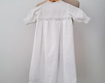 Puede incluir: Vestido de bautizo blanco con ribete de encaje alrededor del cuello, las mangas y el dobladillo.