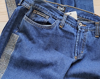 May include: Dark blue denim jeans with a rhinestone embellishment on the side seam. The jeans have a D&G label on the back waistband.