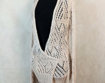 May include: A beige crochet cardigan with a deep V-neck and a tie at the waist.