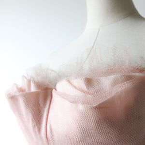 以下が含まれることがあります： チュールを重ねたピンクのストラップレスドレス。ドレスはギャザーの入ったボディスとフィットしたスカートです。