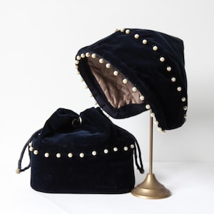 Peut inclure: Un chapeau en velours noir et un sac à cordon assorti, tous deux ornés de petites perles de fantaisie espacées. Le chapeau est présenté sur un support doré, révélant sa doublure intérieure. Le sac a une fermeture à cordon.