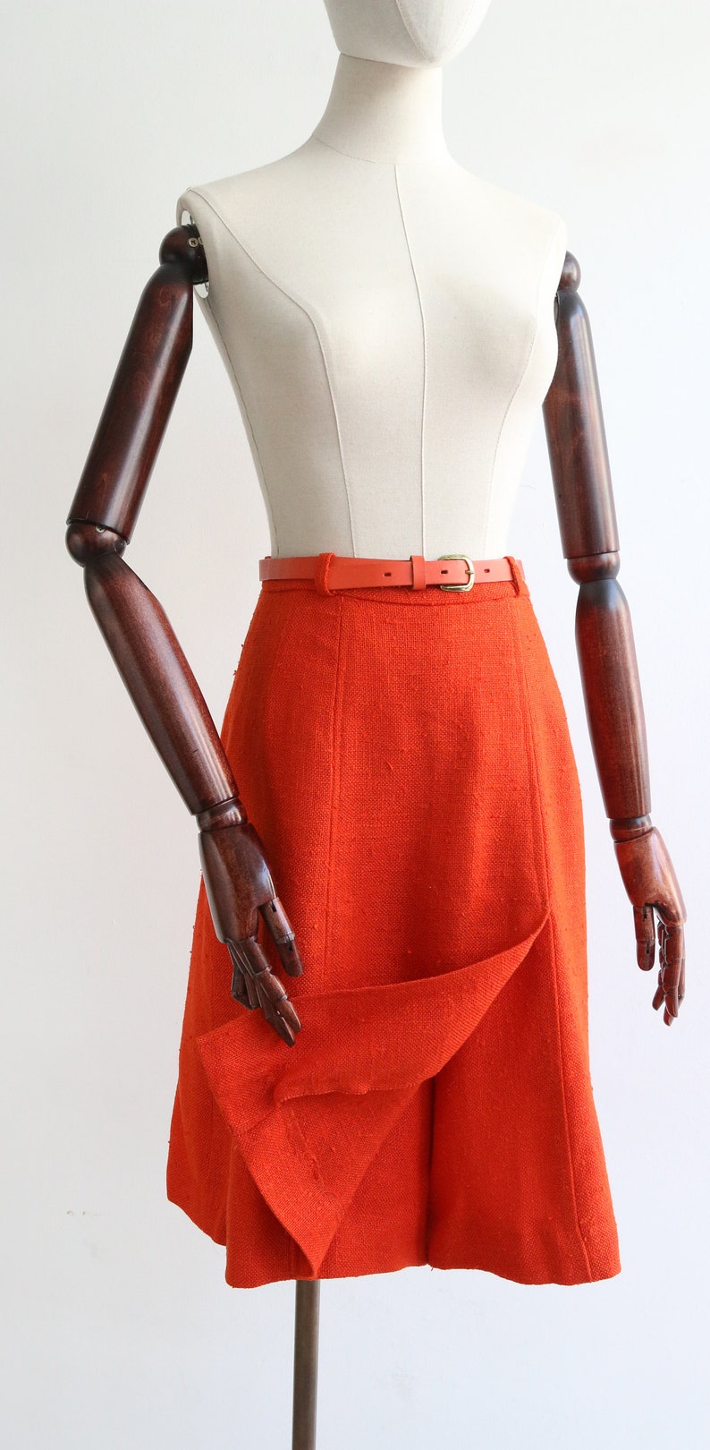 May include: A bright orange skirt with a fitted waist and a slightly flared hem. The skirt is cinched with a thin orange leather belt.