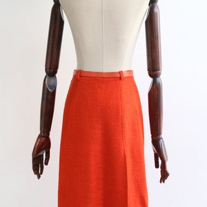 May include: A bright orange skirt with a red belt. The skirt is made of a textured fabric and has a straight silhouette.